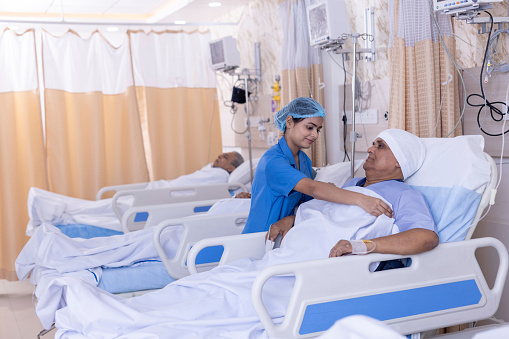 Smiling nurse covering male patient on bed with blanket at hospital ward